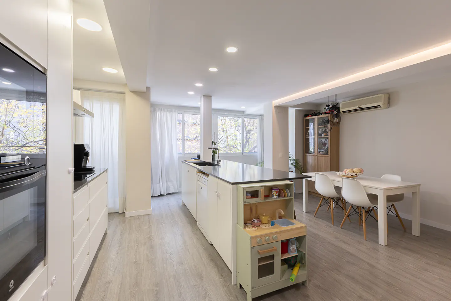 Bright, open-concept kitchen and dining area with white cabinets, island with a toy kitchen, and a white dining table with four chairs.