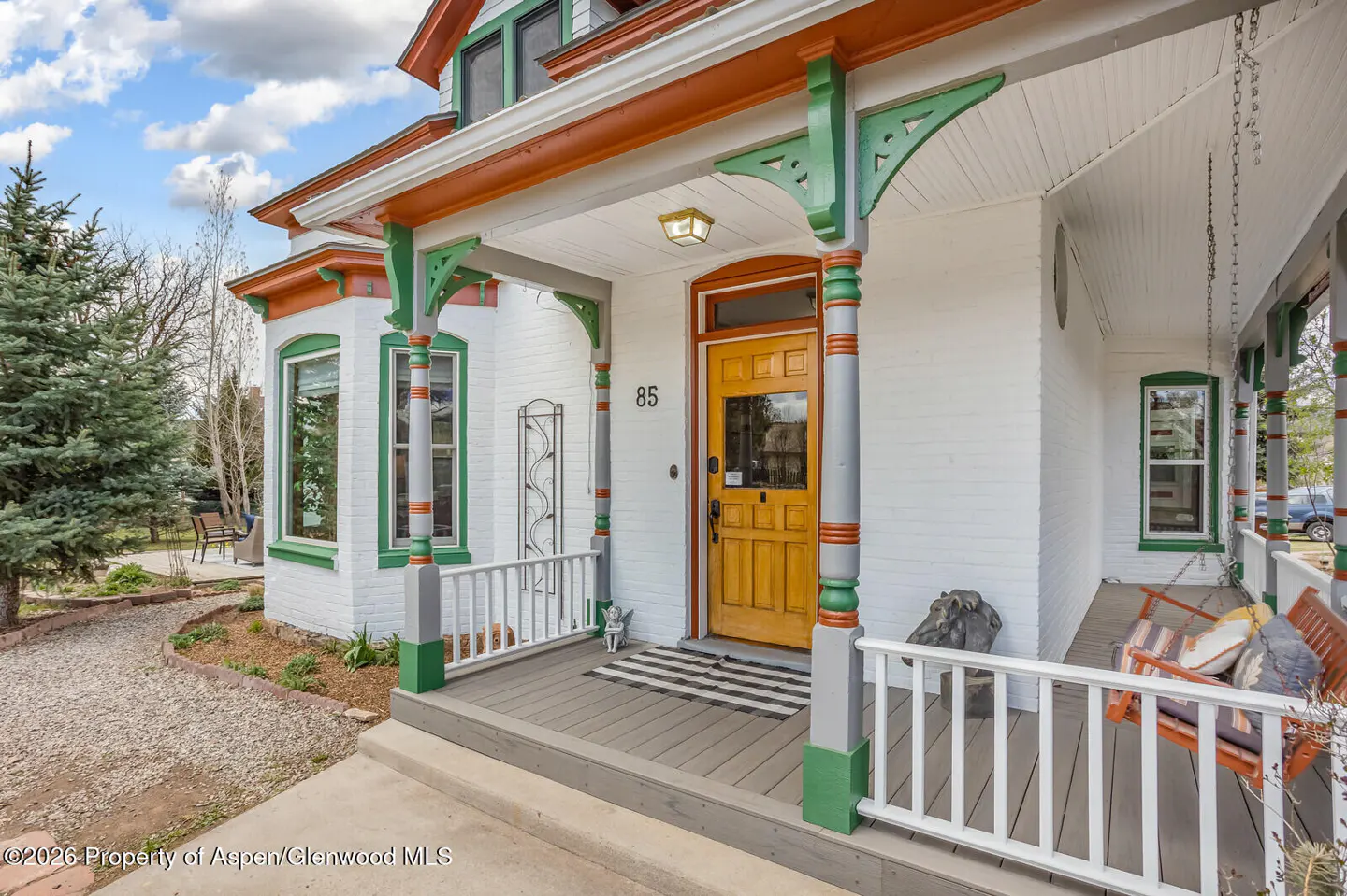 Front porch of a white house with green and orange trim, a yellow door, and a porch swing.