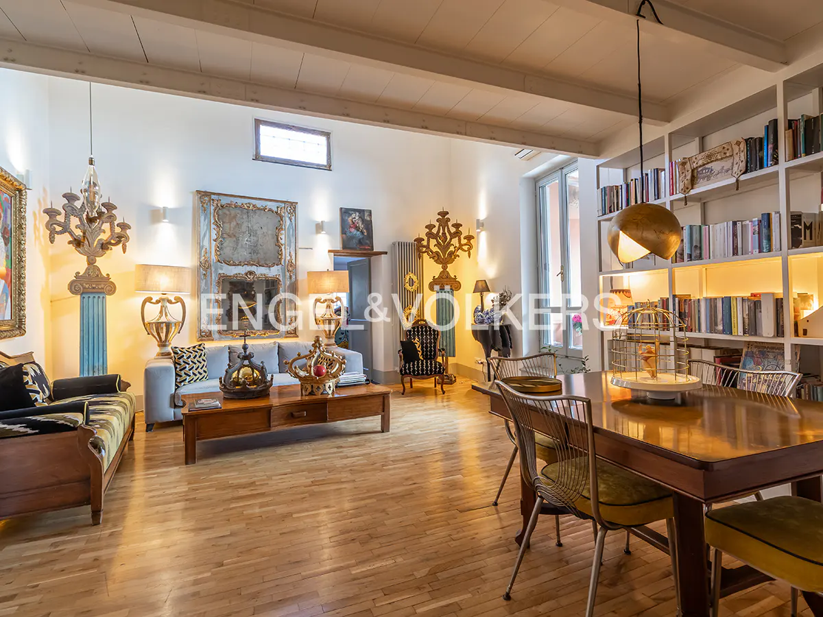 A spacious living and dining area with hardwood floors, sofas, a wooden table, and a bookshelf filled with books.