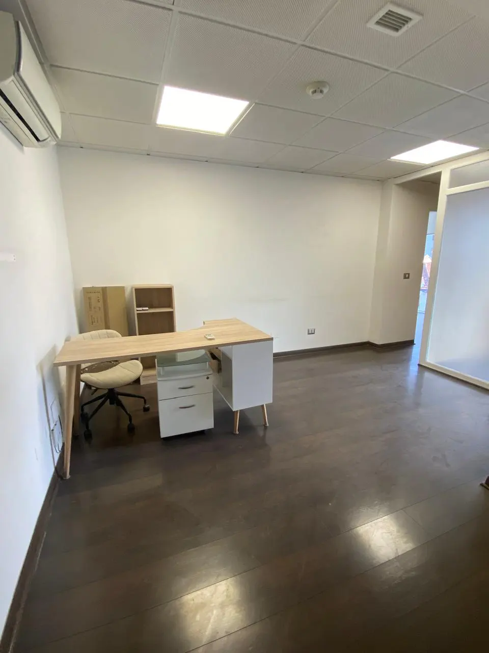 Bright office space with dark wood floors, white walls, and a light wood desk with a white chair.