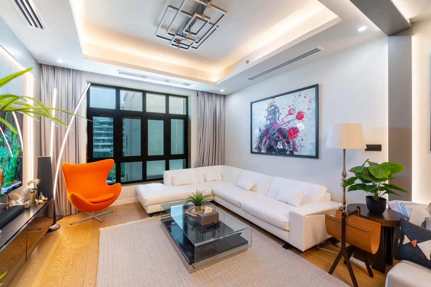 Bright living room with white L-shaped sofa, glass coffee table, orange chair, and large abstract art on the wall.