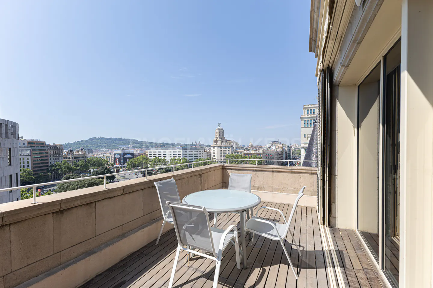 Balcony with a round table and four chairs overlooking a city skyline on a sunny day.
