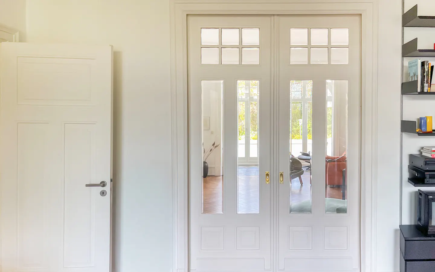 Interior view of a white room with a closed white door and glass paneled double doors. A black bookshelf is on the right.
