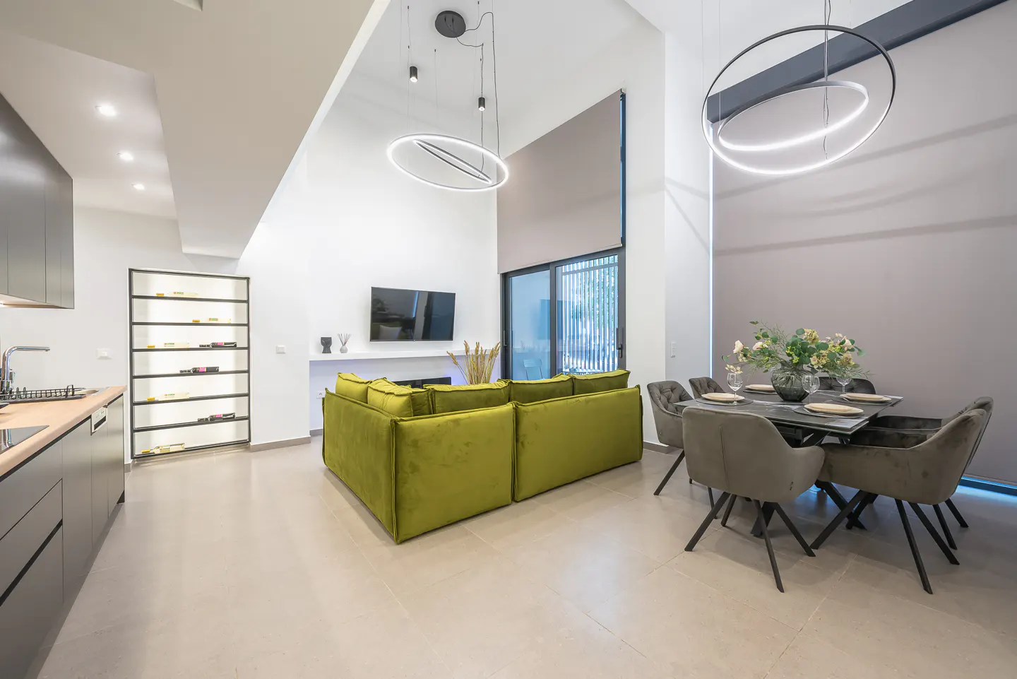 Open-concept living space with a green velvet sofa, dining table, and modern lighting fixtures.