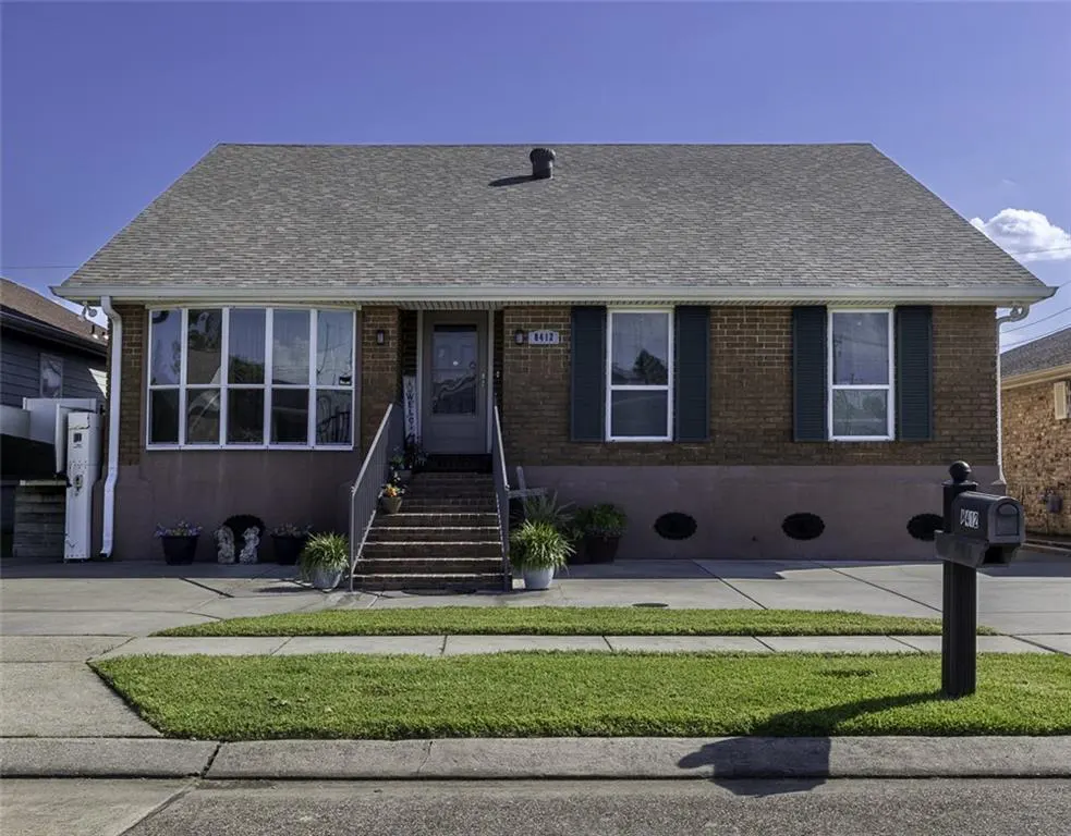 A single-story brick house with green shutters, a gray roof, and a small front yard. A mailbox stands to the right.