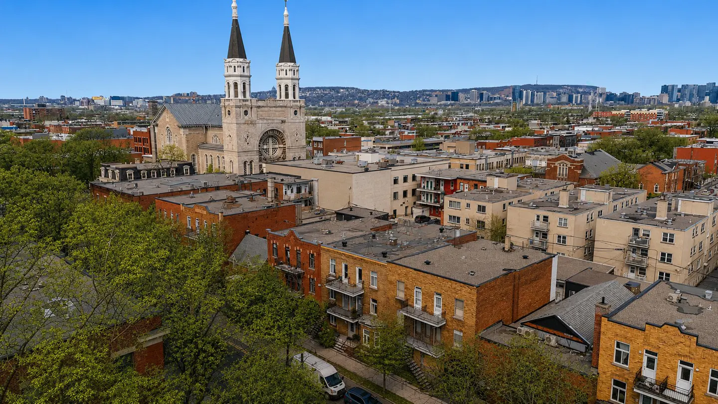Aerial view of Montreal neighborhood with brick buildings, church with two spires, and city skyline.