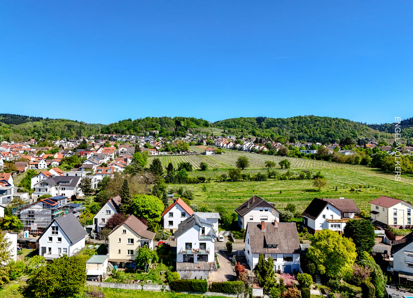 Aerial view of a residential area with houses, green hills, and a clear blue sky.
