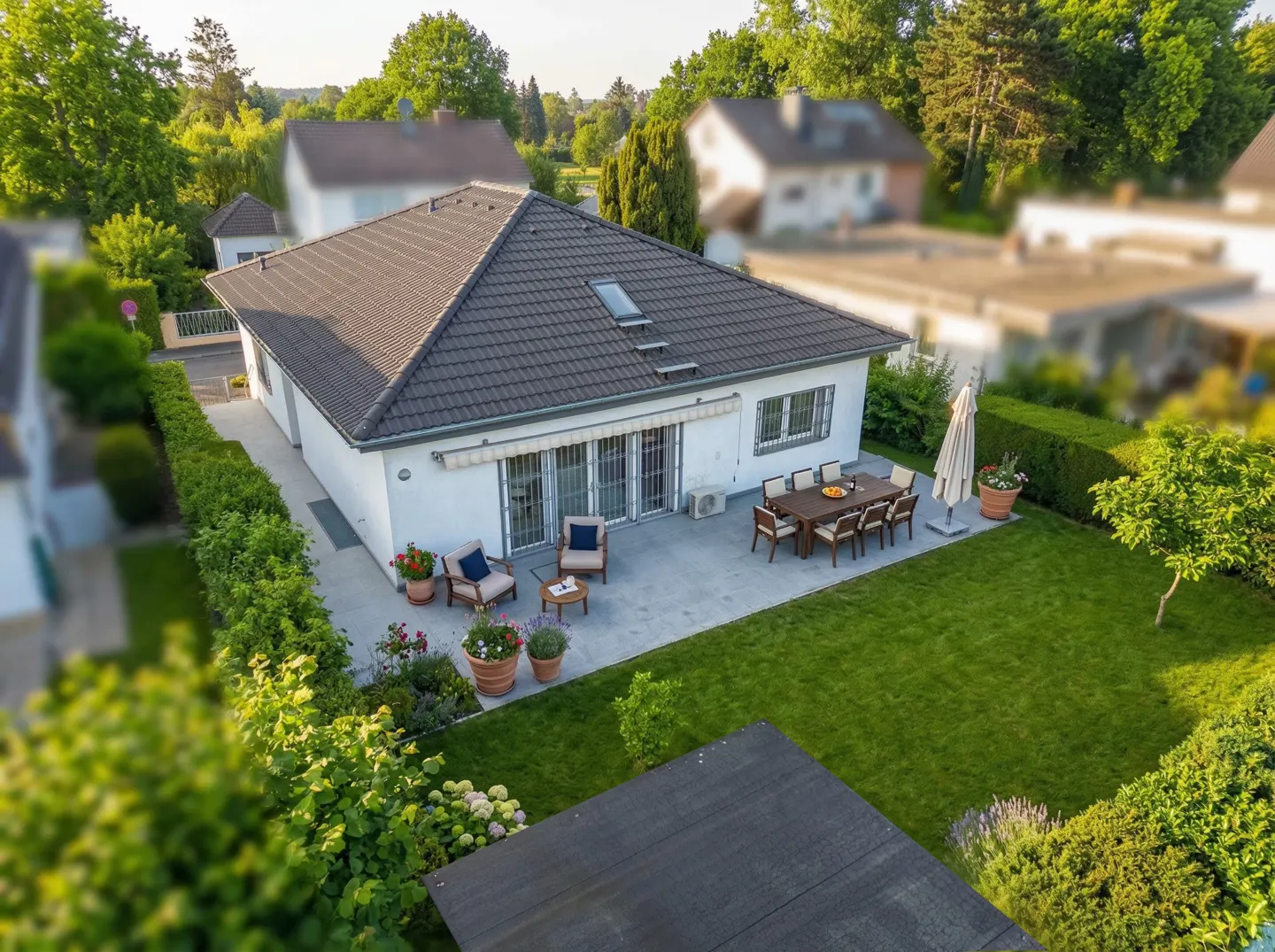 Aerial view of a white house with a brown roof, patio furniture, and a green lawn.