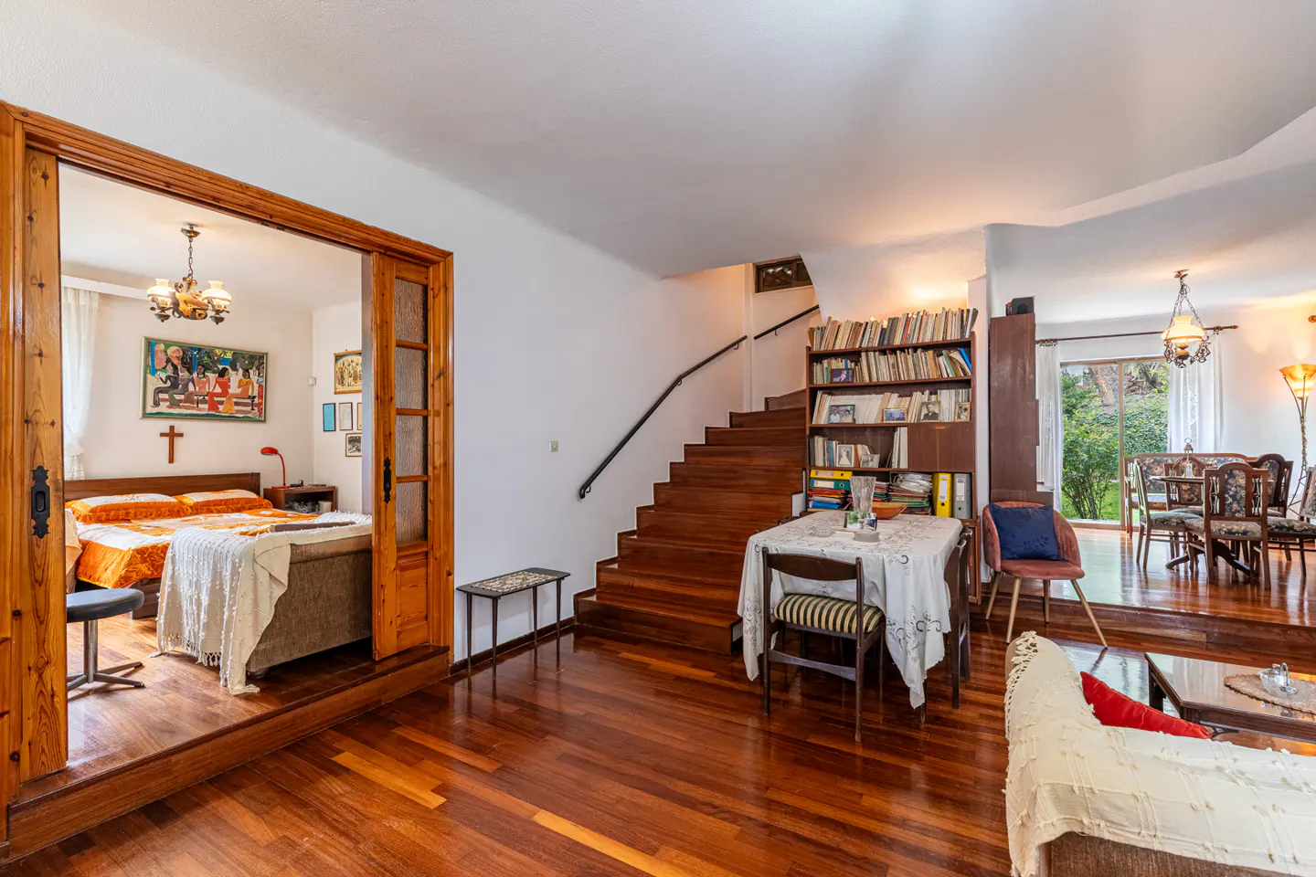 Open-concept living space with hardwood floors, stairs, and a bedroom visible through a wood-framed doorway.