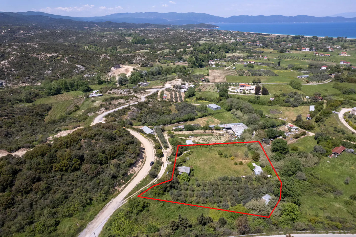 Aerial view of a property outlined in red, surrounded by green hills, with a blue sea in the background.