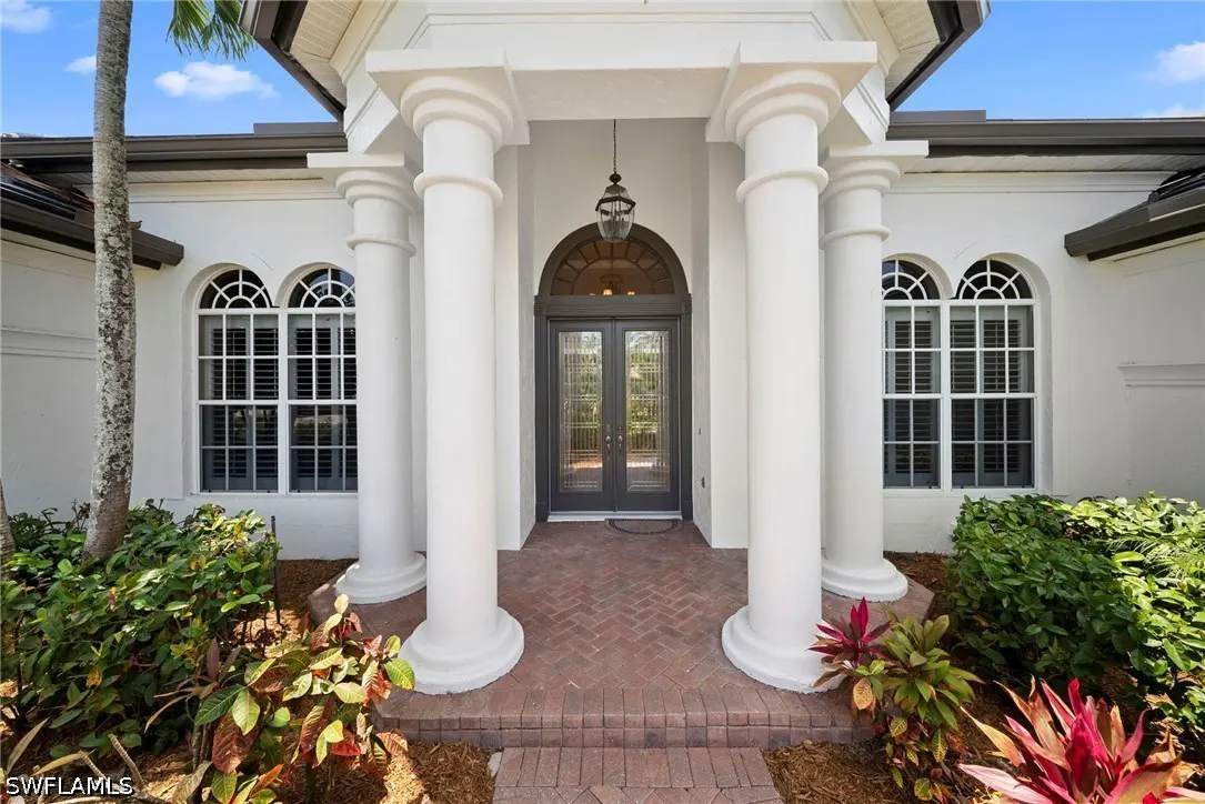 Exterior of a white house with a brick walkway leading to a double door entrance framed by white columns. Arched windows flank the entrance.