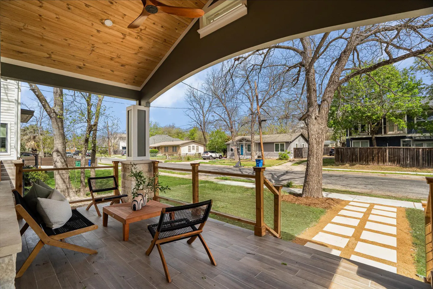 Covered porch with wood ceiling, ceiling fan, stone columns, and gray tile floor. Outdoor furniture includes chairs and a coffee table.