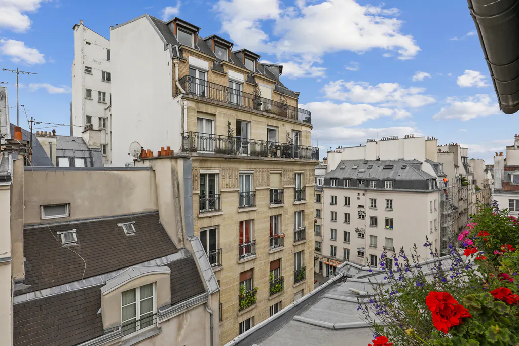 View of classic Parisian apartment buildings with stone facades, balconies, and slate roofs under a blue sky with clouds.