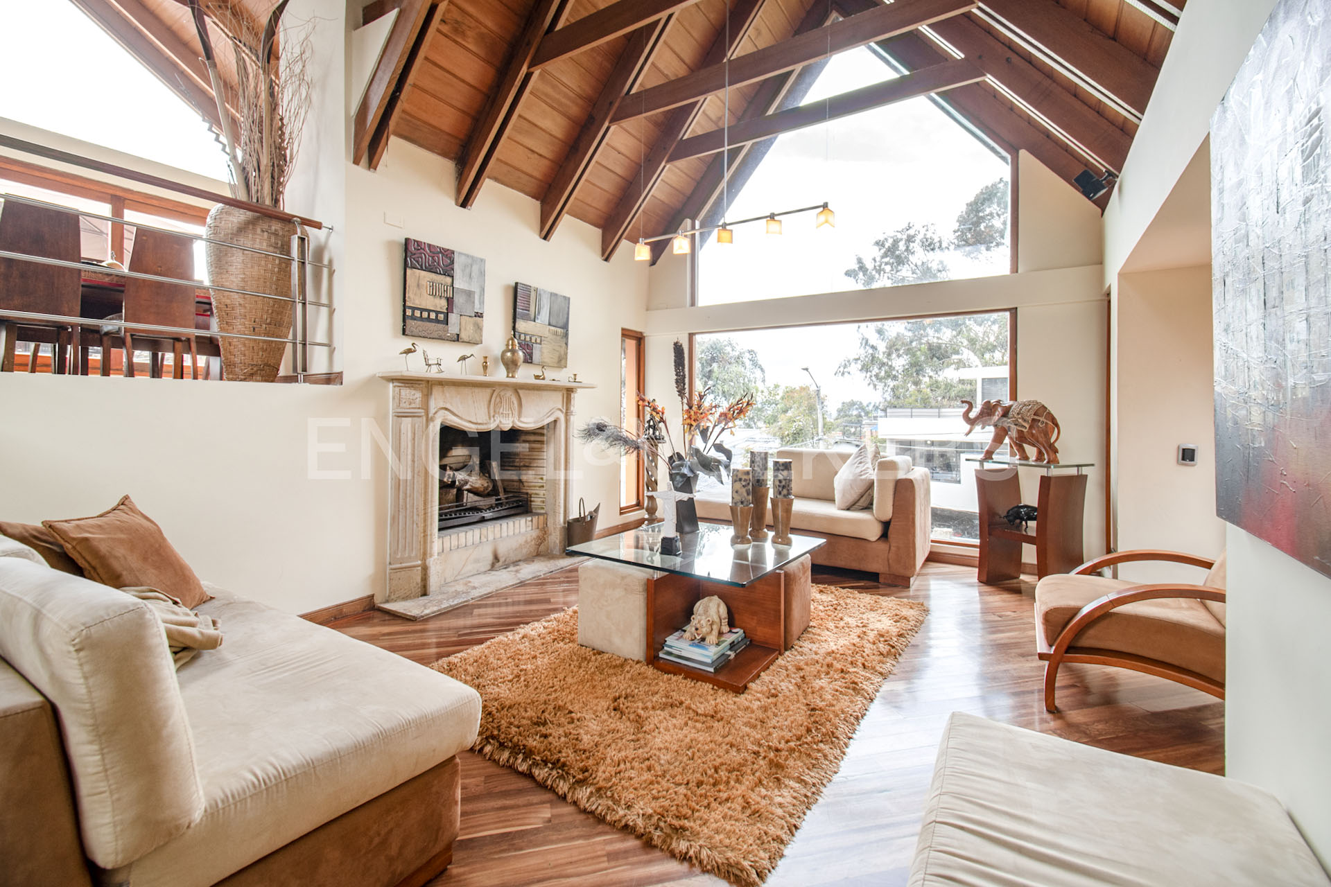 Spacious living room with vaulted wood ceiling, stone fireplace, beige sofas, glass coffee table, and large windows. [AI-generated text]