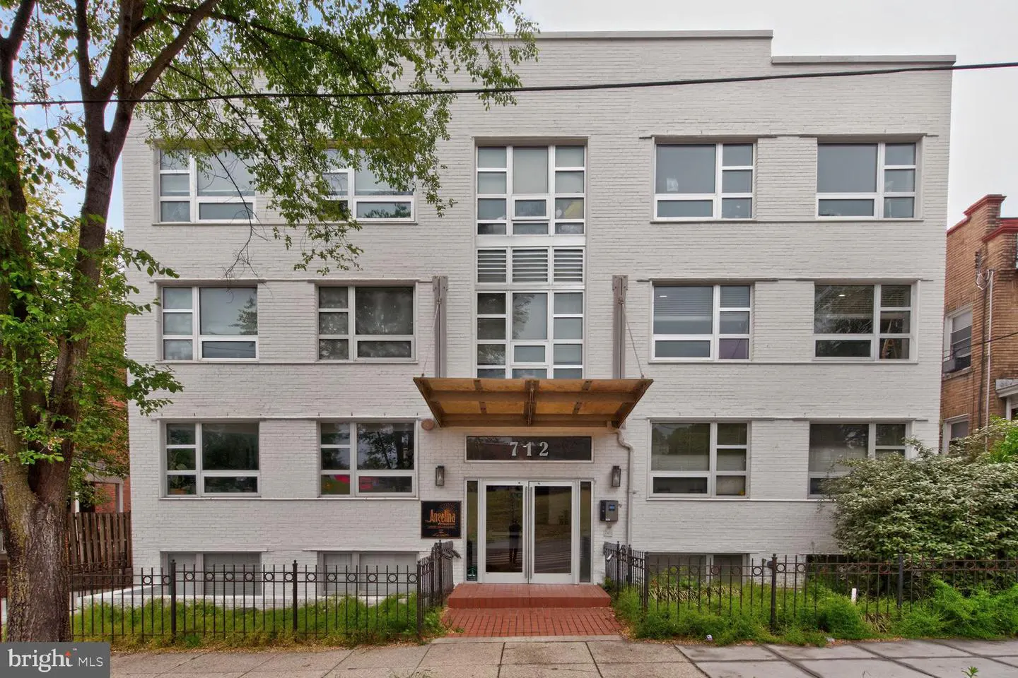 Exterior of a four-story white brick apartment building with a brown awning over the entrance. Address 712 is above the door.