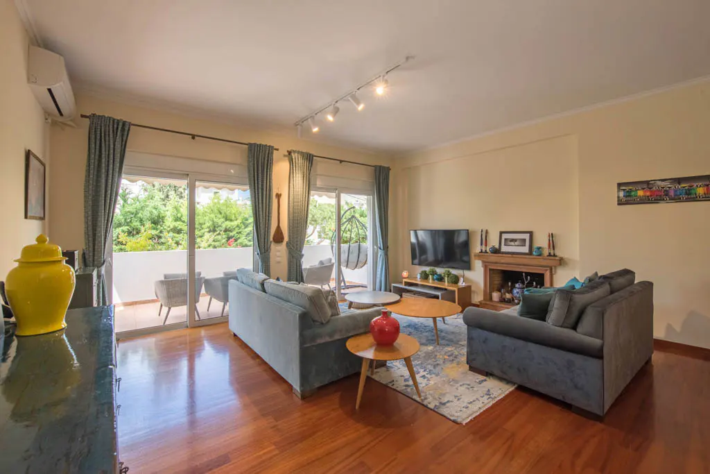 A living room with hardwood floors, two blue sofas, a fireplace, and a balcony with outdoor furniture.