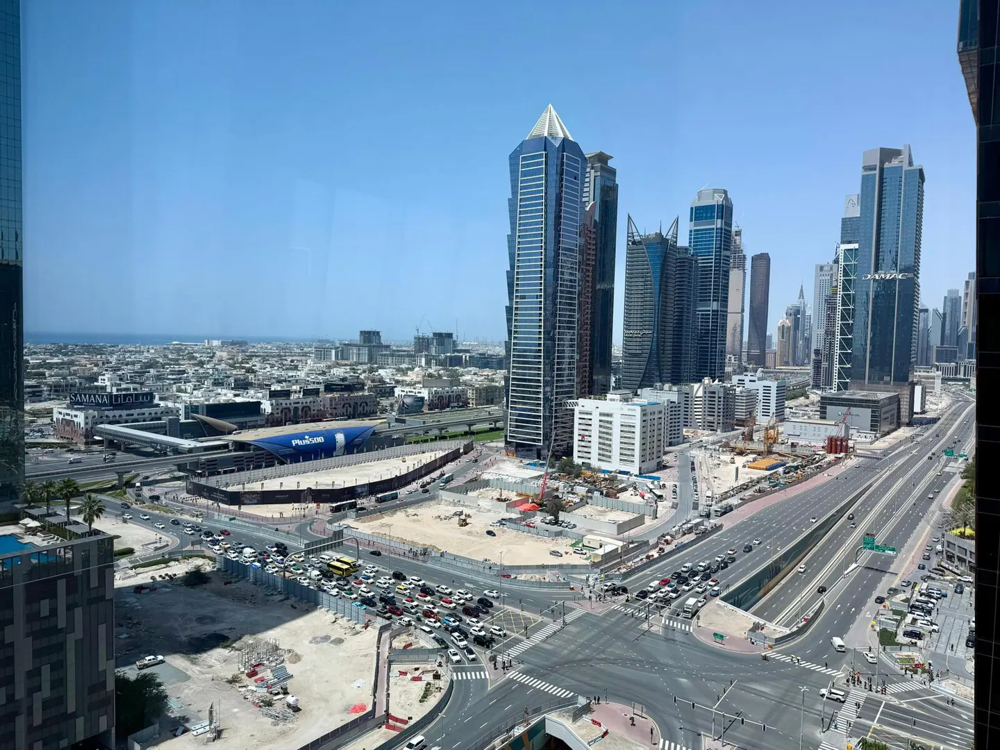 View of Dubai skyline with modern skyscrapers, busy roads, and construction sites under a clear blue sky.