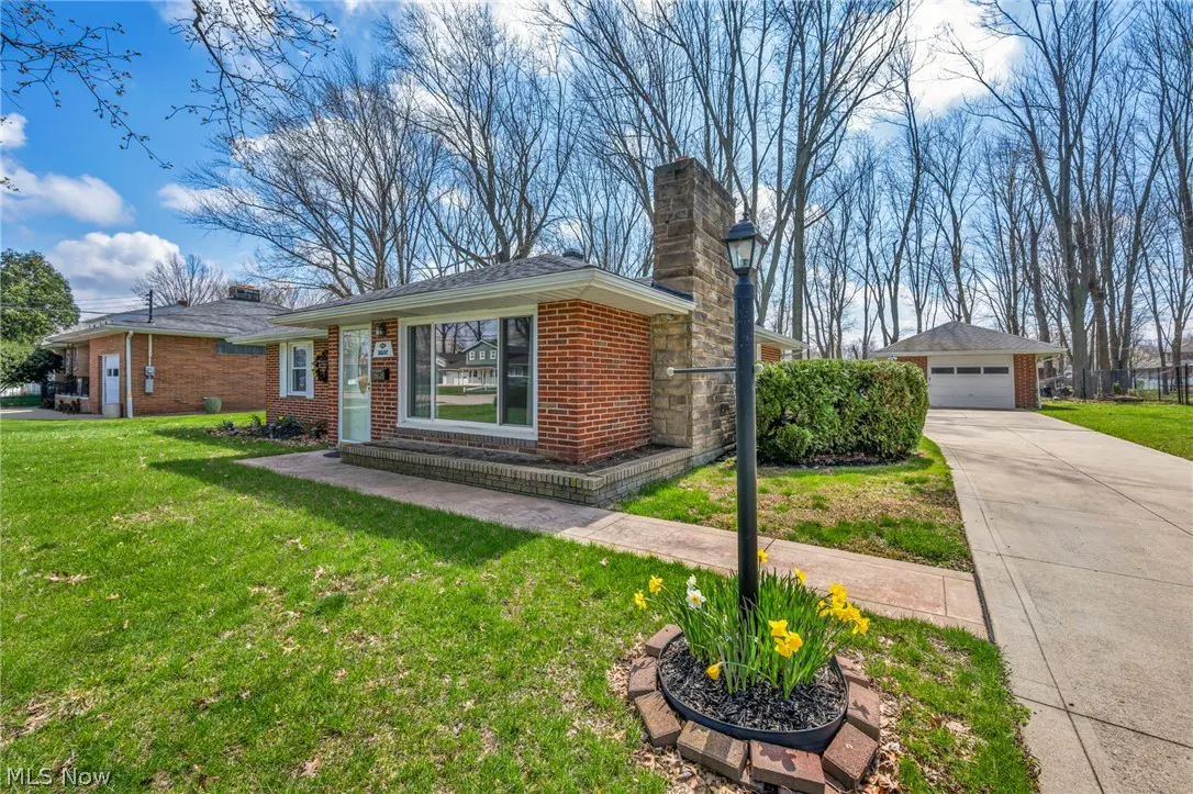 A single-story red brick house with a stone chimney, green lawn, and a lamp post with yellow flowers.