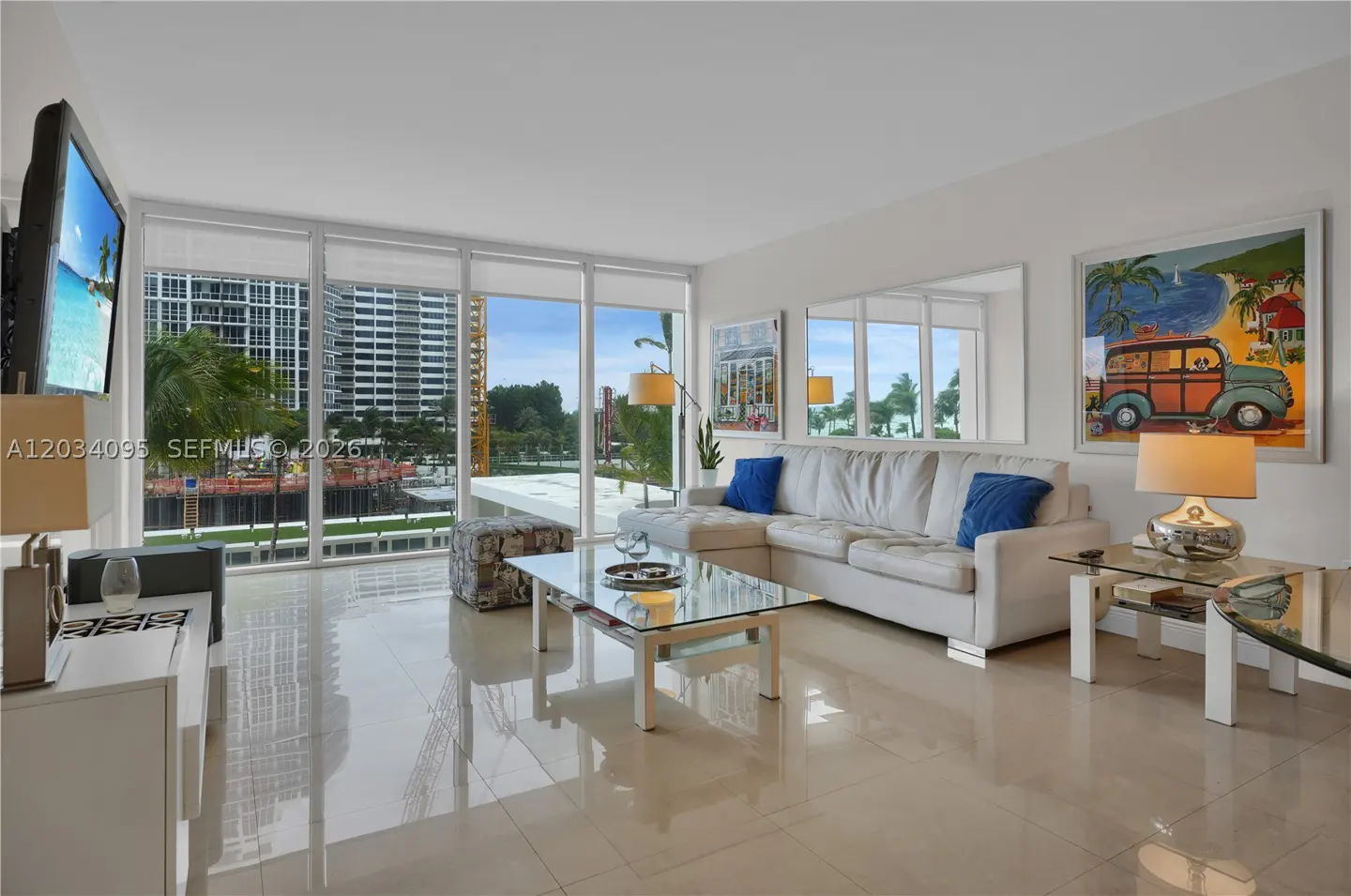 Modern living room with white sofa, glass coffee table, and large windows overlooking a city construction site.