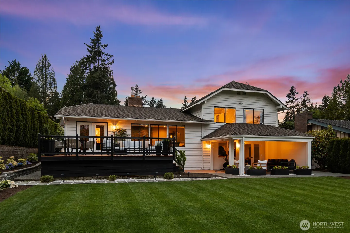 Exterior shot of a white two-story house with a black deck and green lawn at dusk.