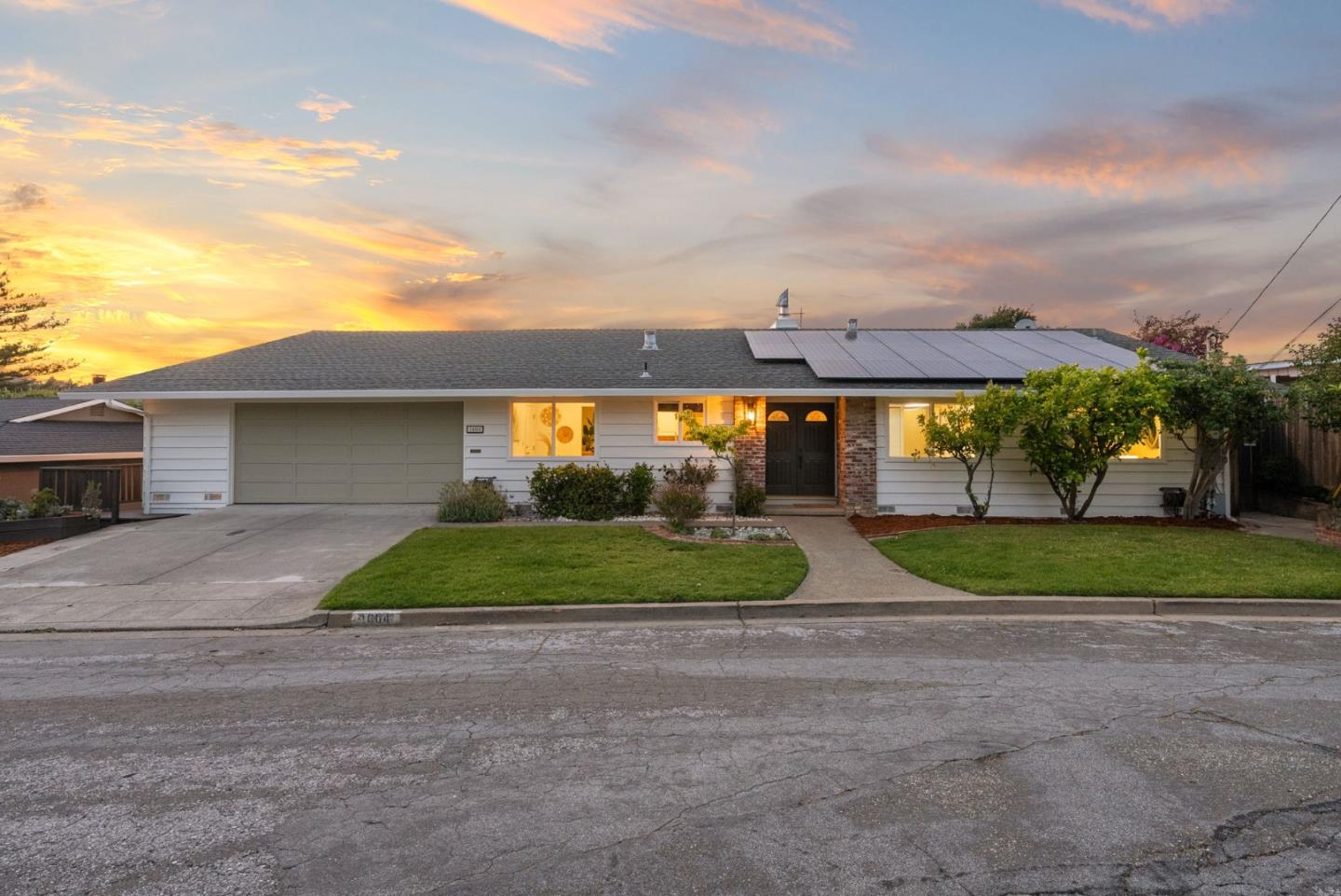 A white single-story house with a gray roof and solar panels at sunset.