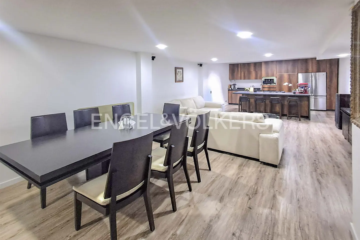 Open-concept living space with a dark wood dining table, white sofas, and a kitchen island with bar stools.