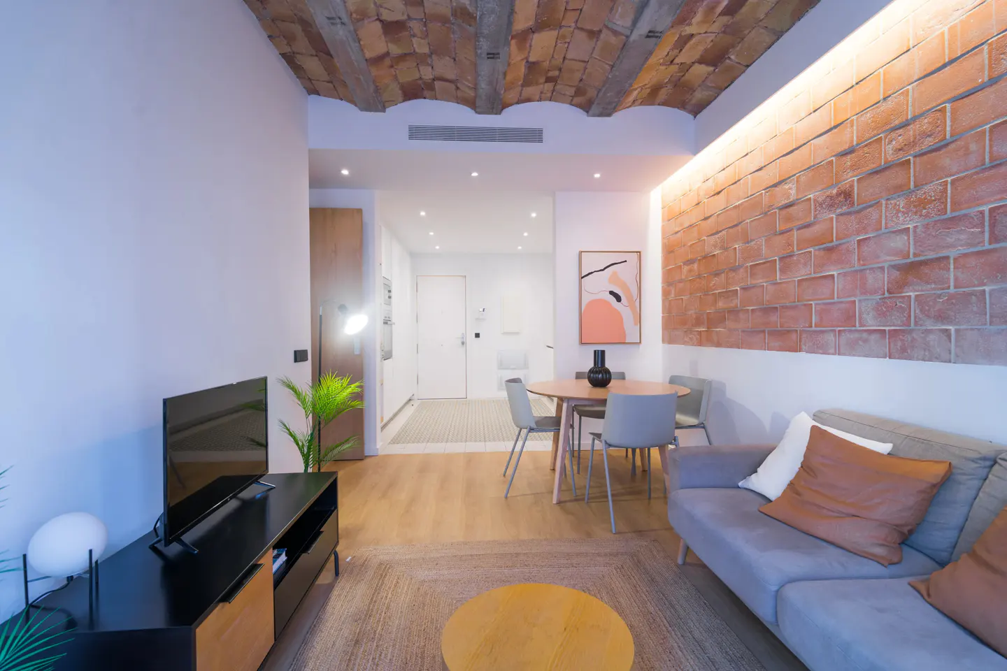 Living room with brick wall and ceiling, gray sofa, round table with chairs, and TV stand. Modern interior design.