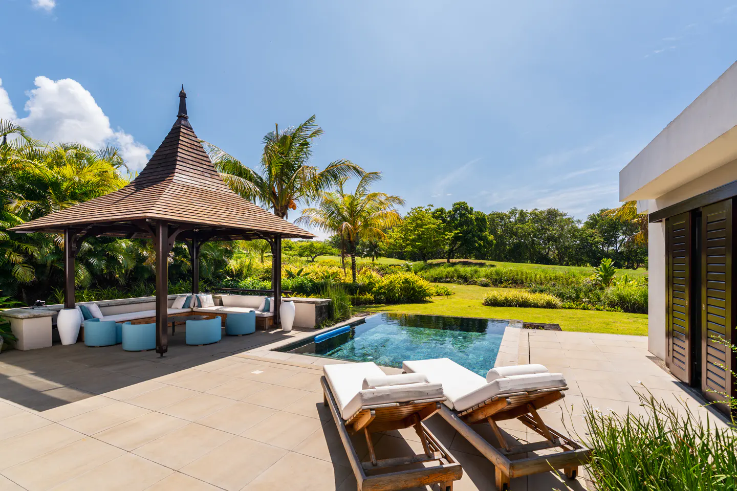 Outdoor patio with a gazebo, pool, and lounge chairs on a sunny day.