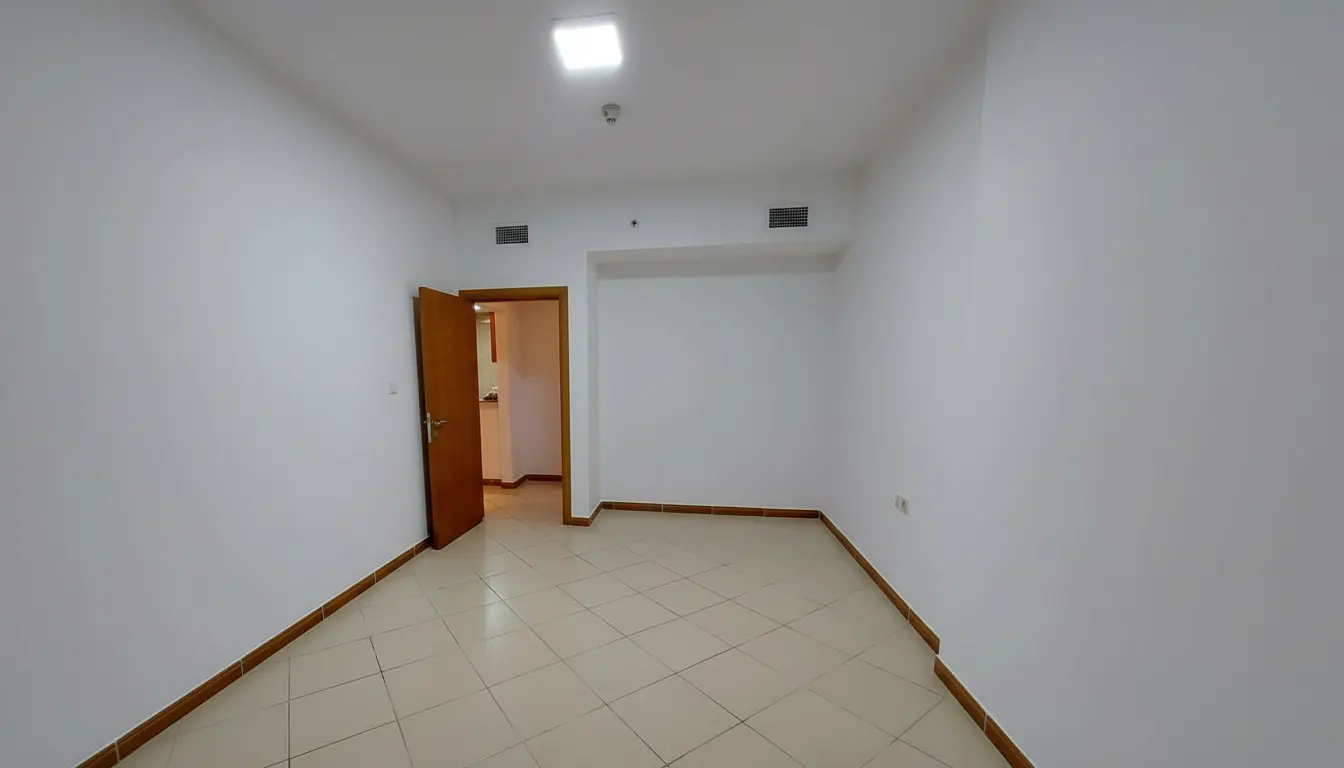 A vacant room with white walls, beige tile floor, and an open wooden door.