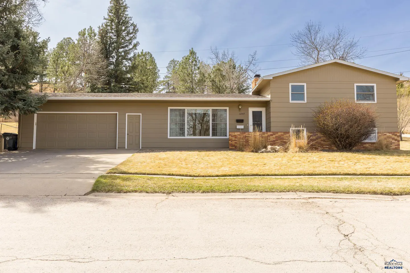 Tan two-story house with an attached garage and a brown door, with a lawn and trees in the background.