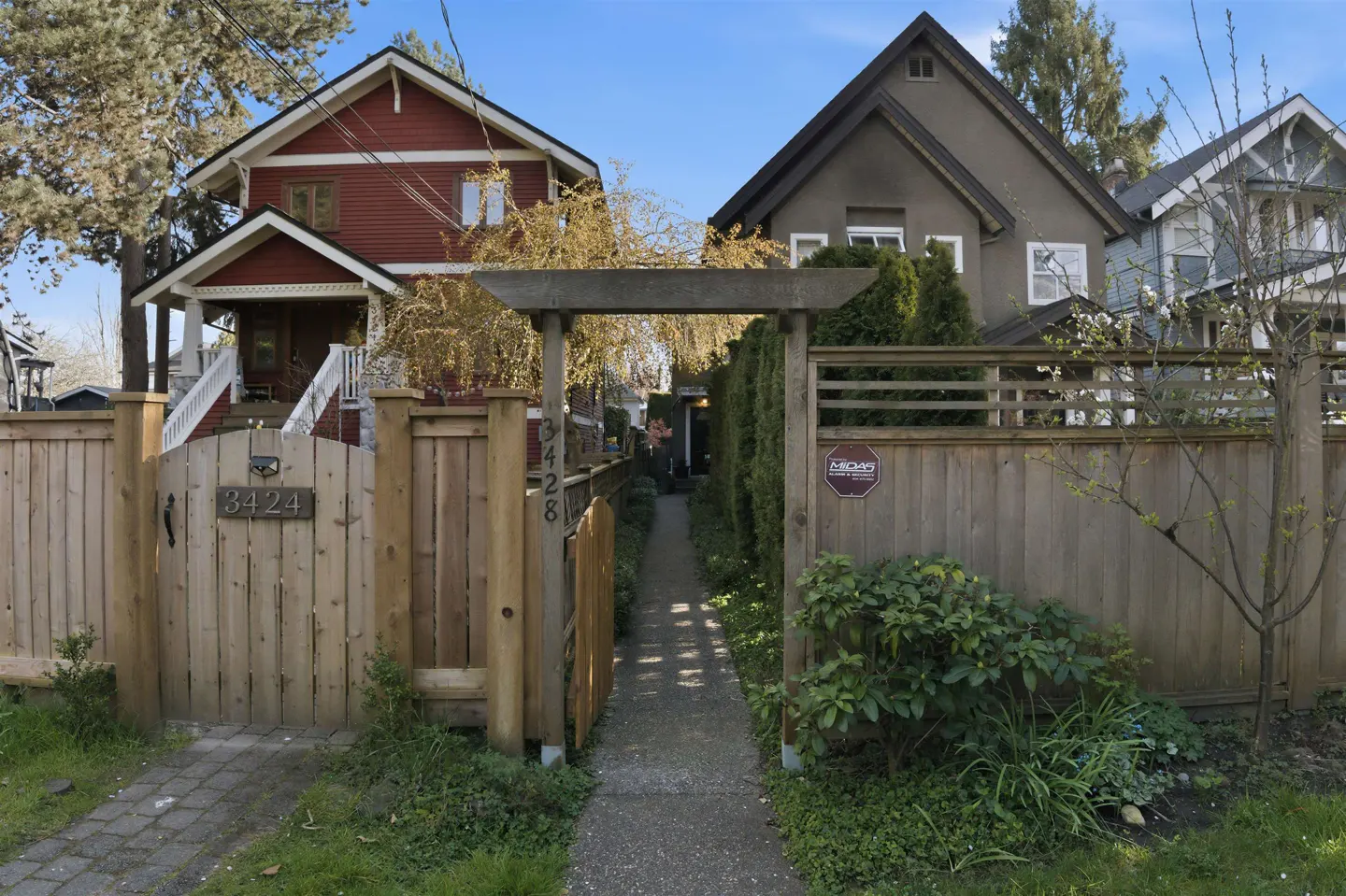 Exterior view of two houses with wooden fences and a walkway between them. The house on the left is red, and the house on the right is gray.