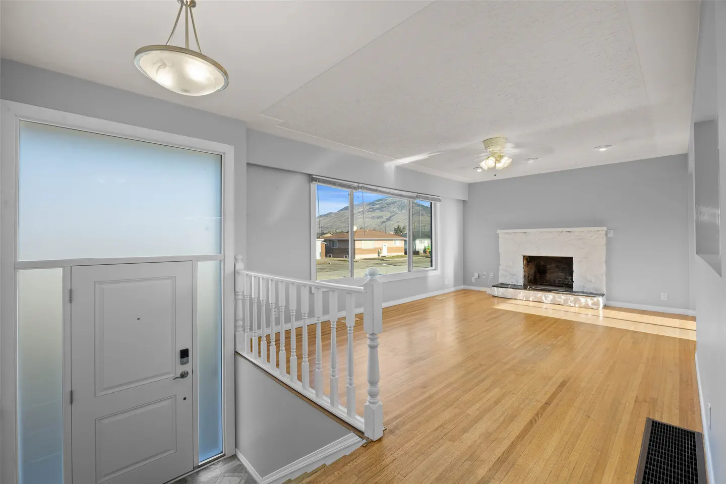 Bright, open-concept home interior with hardwood floors, white trim, and gray walls. A white door with frosted glass is on the left. A fireplace and large window are in the background.