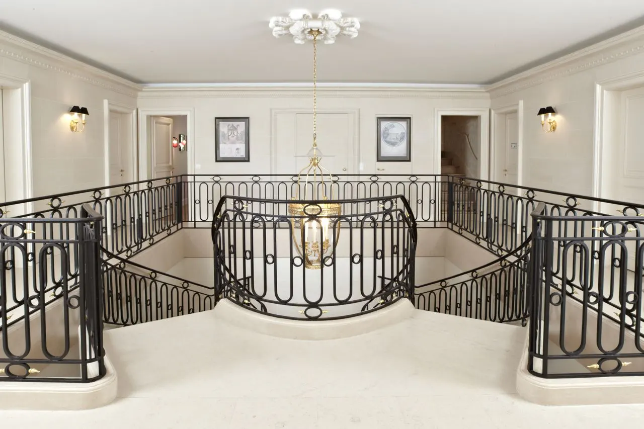 Elegant foyer with black iron railings, cream walls, and a chandelier. Doors and framed art add to the luxurious ambiance.