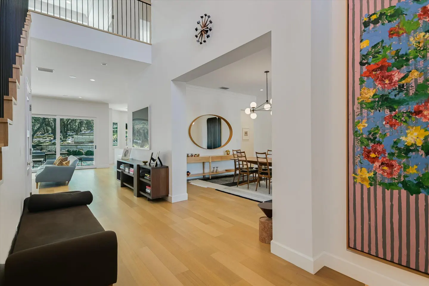 Bright, modern home foyer with light wood floors, white walls, and an open floor plan. A colorful floral painting hangs on the right.