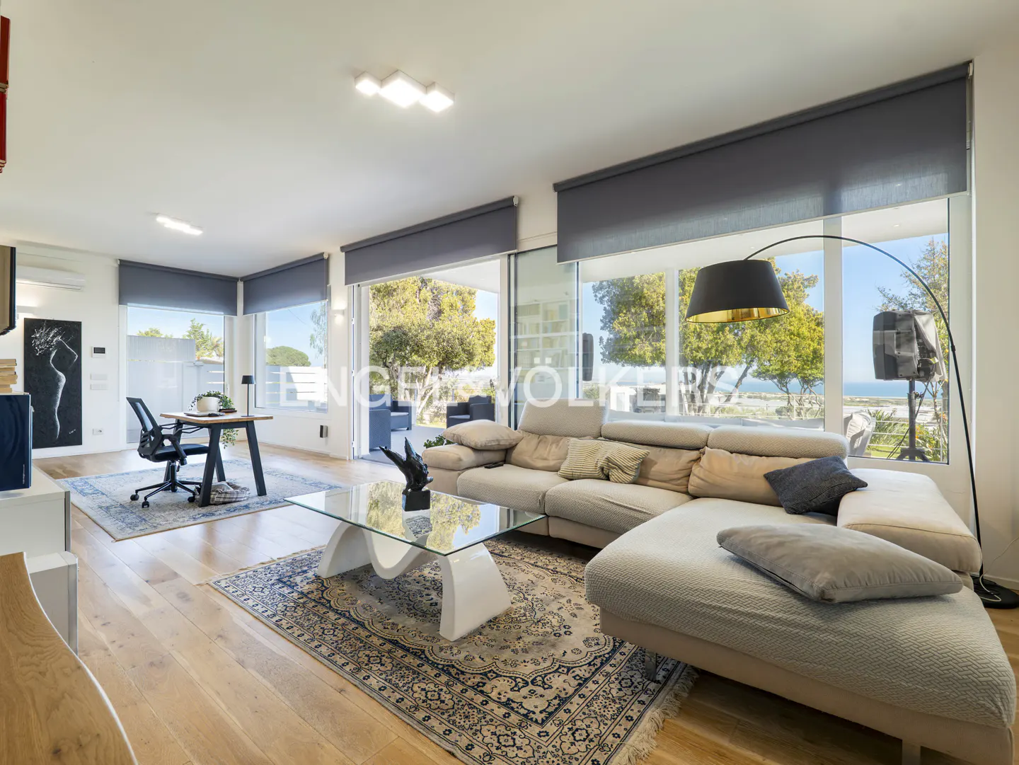 Bright living room with a beige sectional sofa, glass coffee table, and large windows overlooking a green landscape.