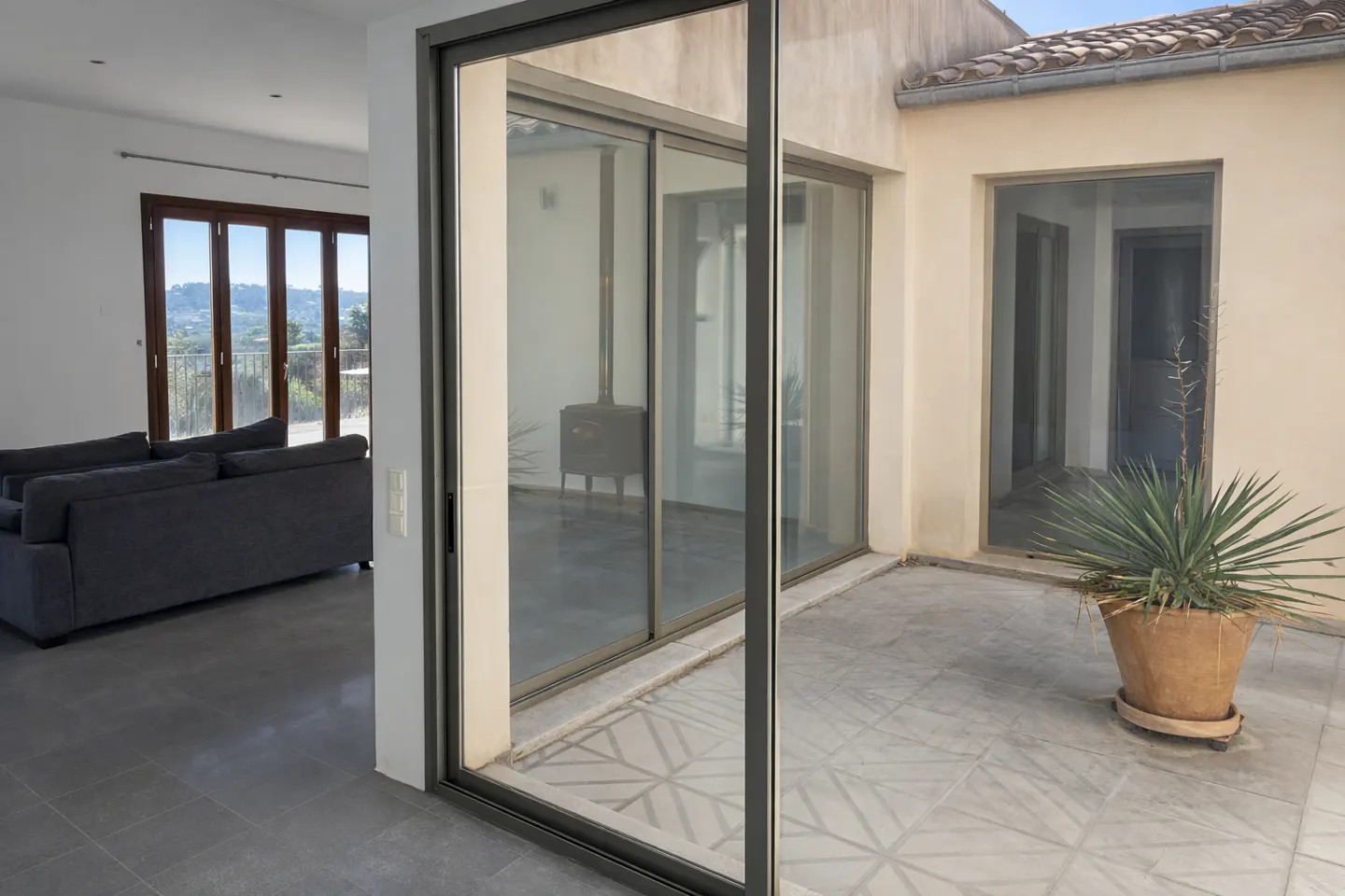 Interior view of a home with sliding glass doors leading to a patio with a potted plant. A gray sofa is visible in the living room.