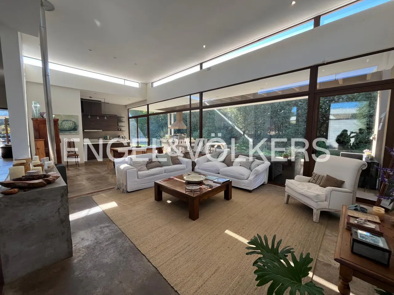 Bright living room with two white sofas, a wooden coffee table on a jute rug, and a white armchair near large windows.