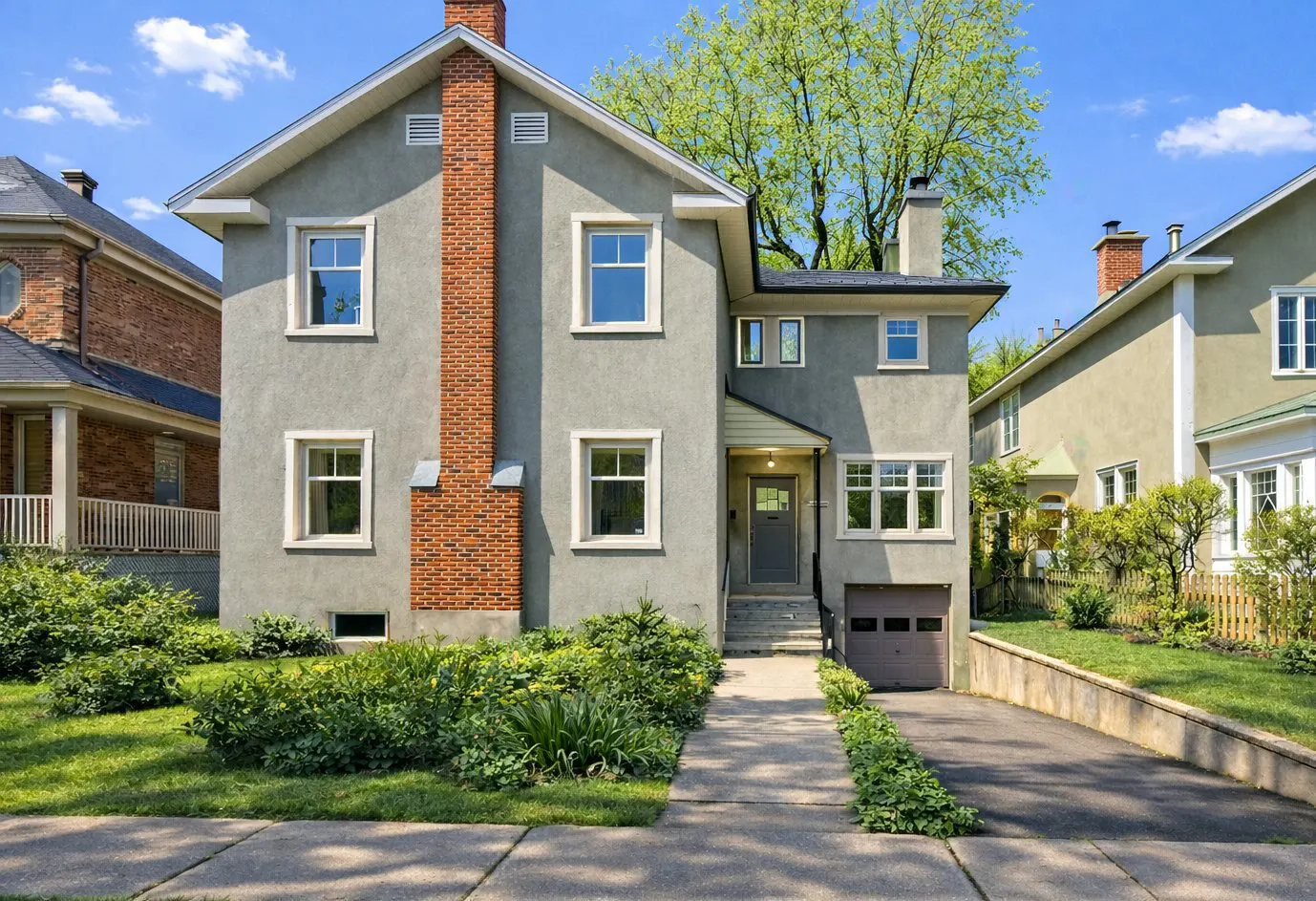 Two-story gray house with a brick chimney, white trim, and a gray front door. A driveway leads to an attached garage.