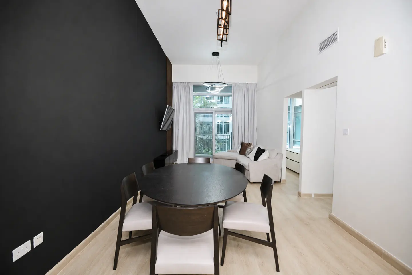 A modern apartment interior with a black accent wall, a round dining table with six chairs, and a white sofa near a window.