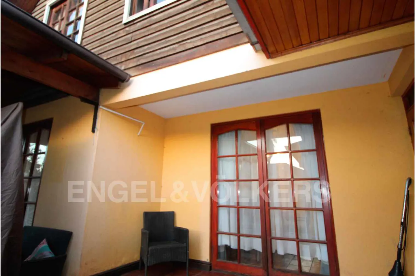 A yellow-walled patio with a dark chair, French doors, and a partial view of a wood-sided house.