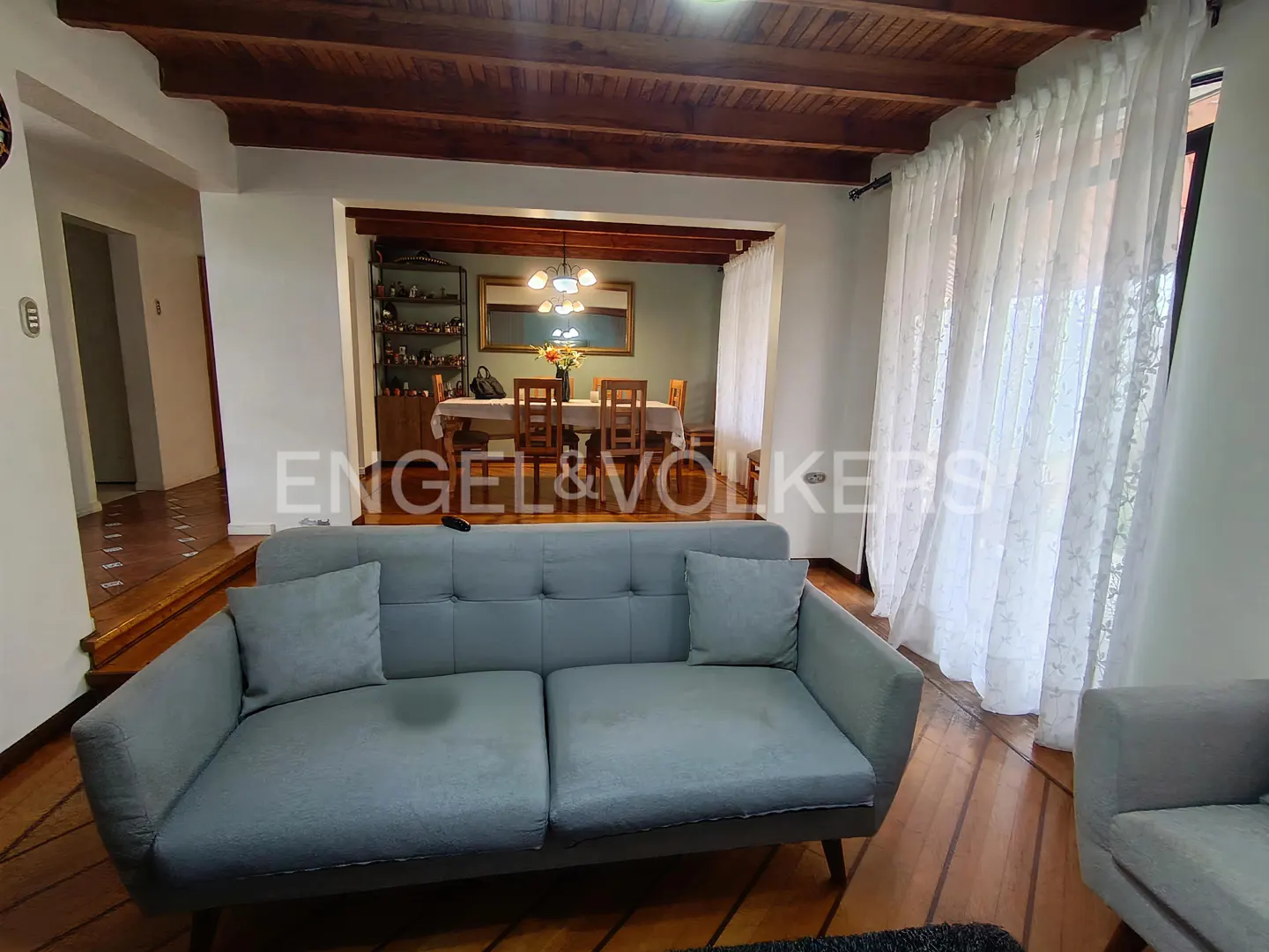 Light blue sofa in a living room with wood-beamed ceilings, looking toward a dining area with a table and chairs.