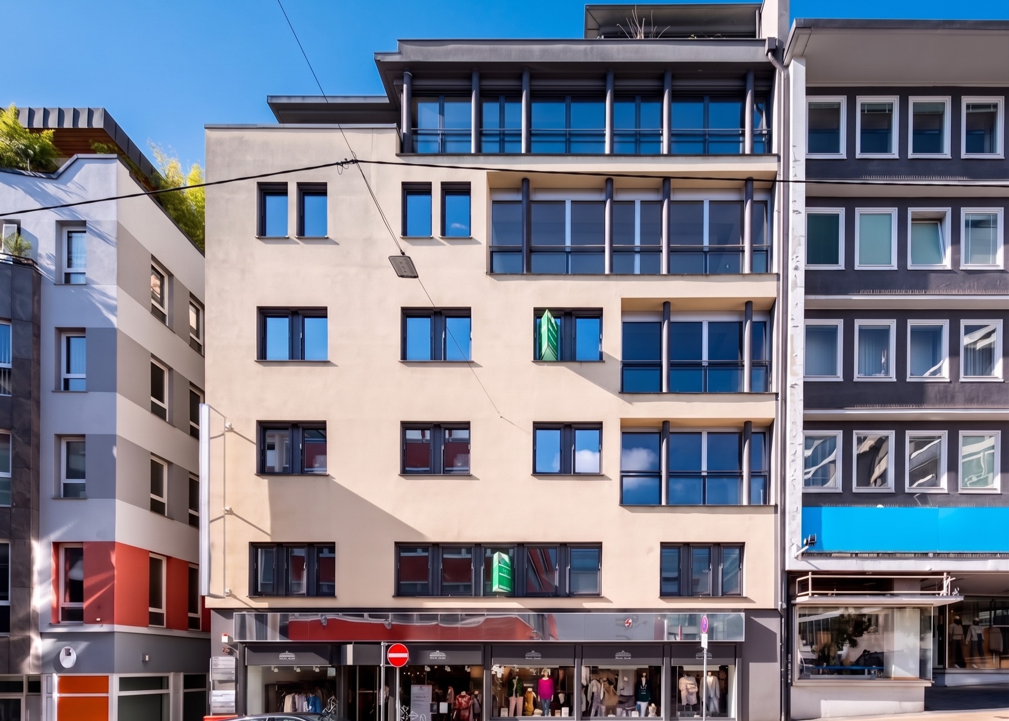 A beige multi-story commercial building with large windows and a ground-floor retail shop under a clear blue sky. [AI-generated text]