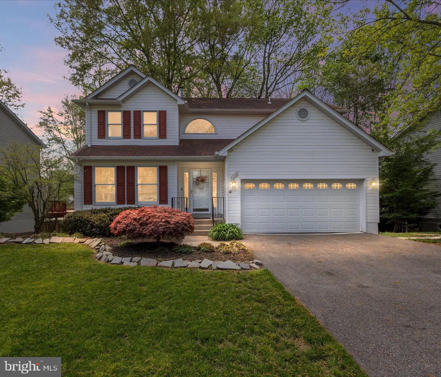 Two-story white house with red shutters, a two-car garage, and a green lawn at dusk.