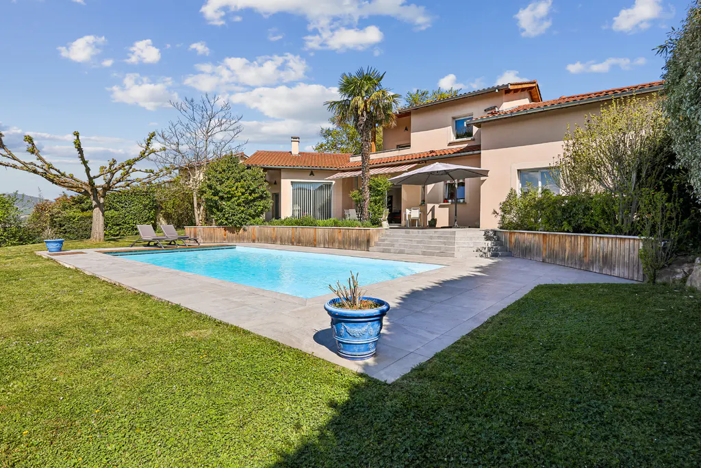 A backyard with a pool, a patio with an umbrella, and a two-story house with a red tile roof.
