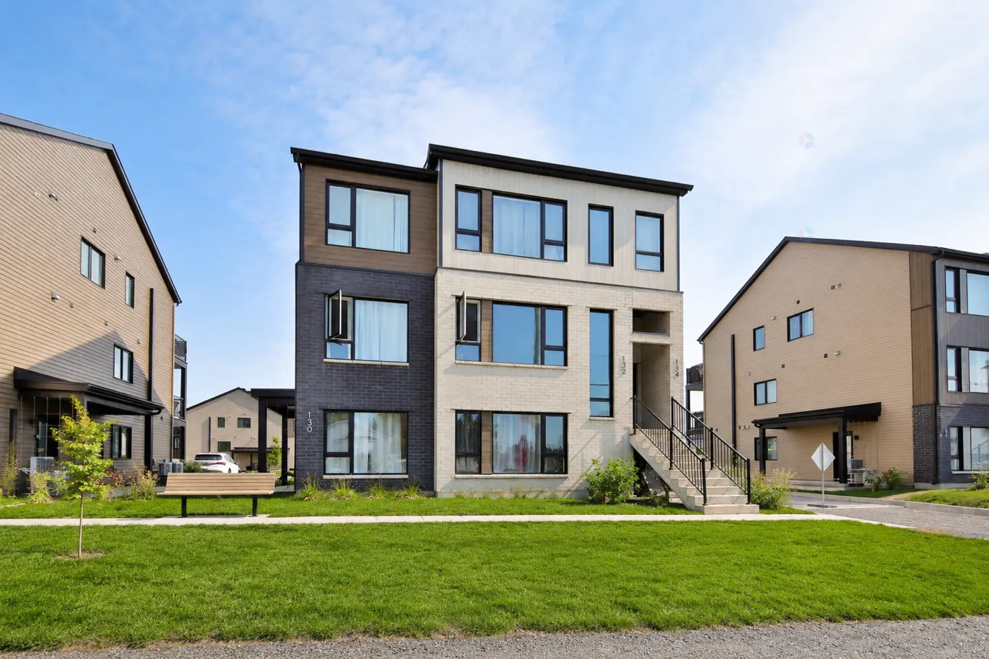 Modern two-story townhouse with black brick and light beige facade, black trim, and a small staircase leading to the entrance.