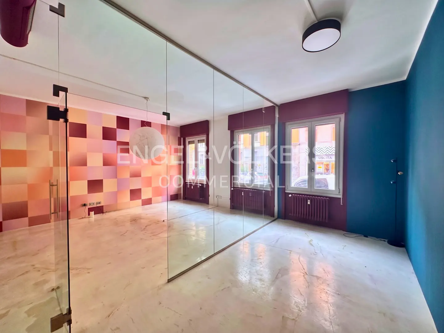 Bright room with marble floors, divided by a glass wall. One side has a pink checkered wall, the other is blue. Two windows are visible.