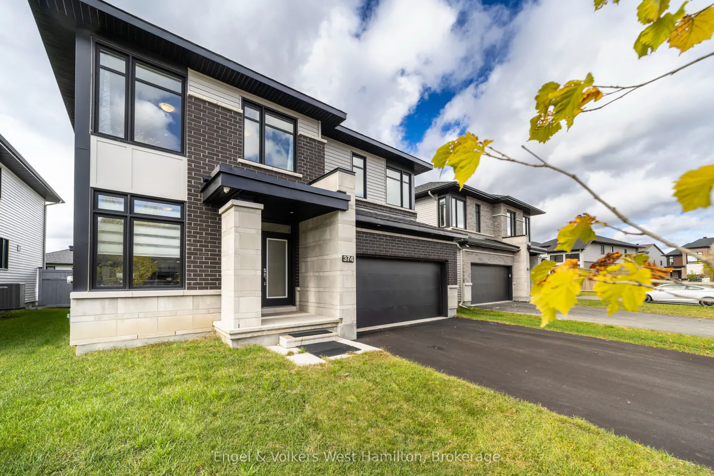 Modern two-story home with black brick, light gray siding, black trim, and a black garage door on a green lawn.