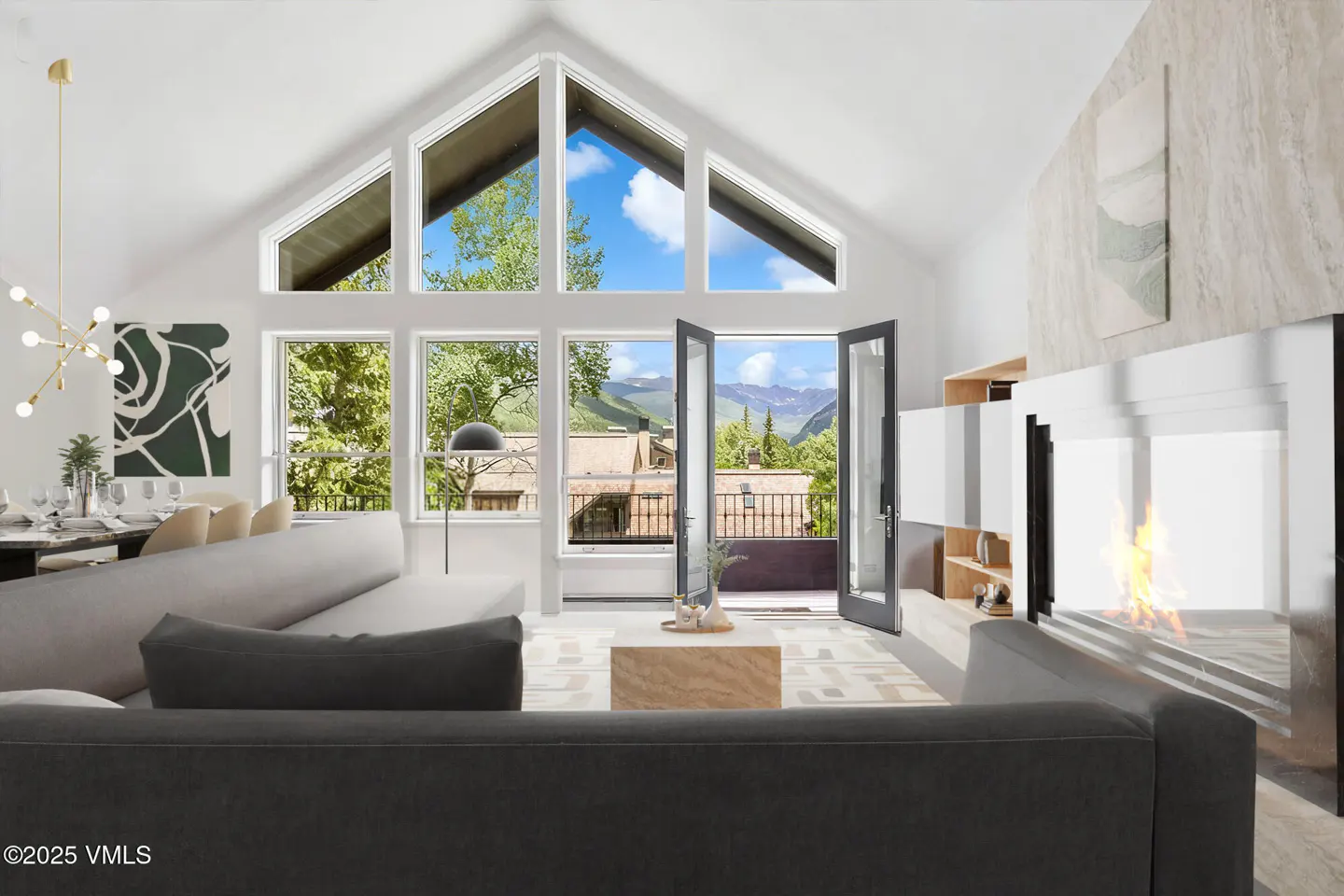 Bright living room with vaulted ceilings, large windows showing mountain views, and a modern fireplace.