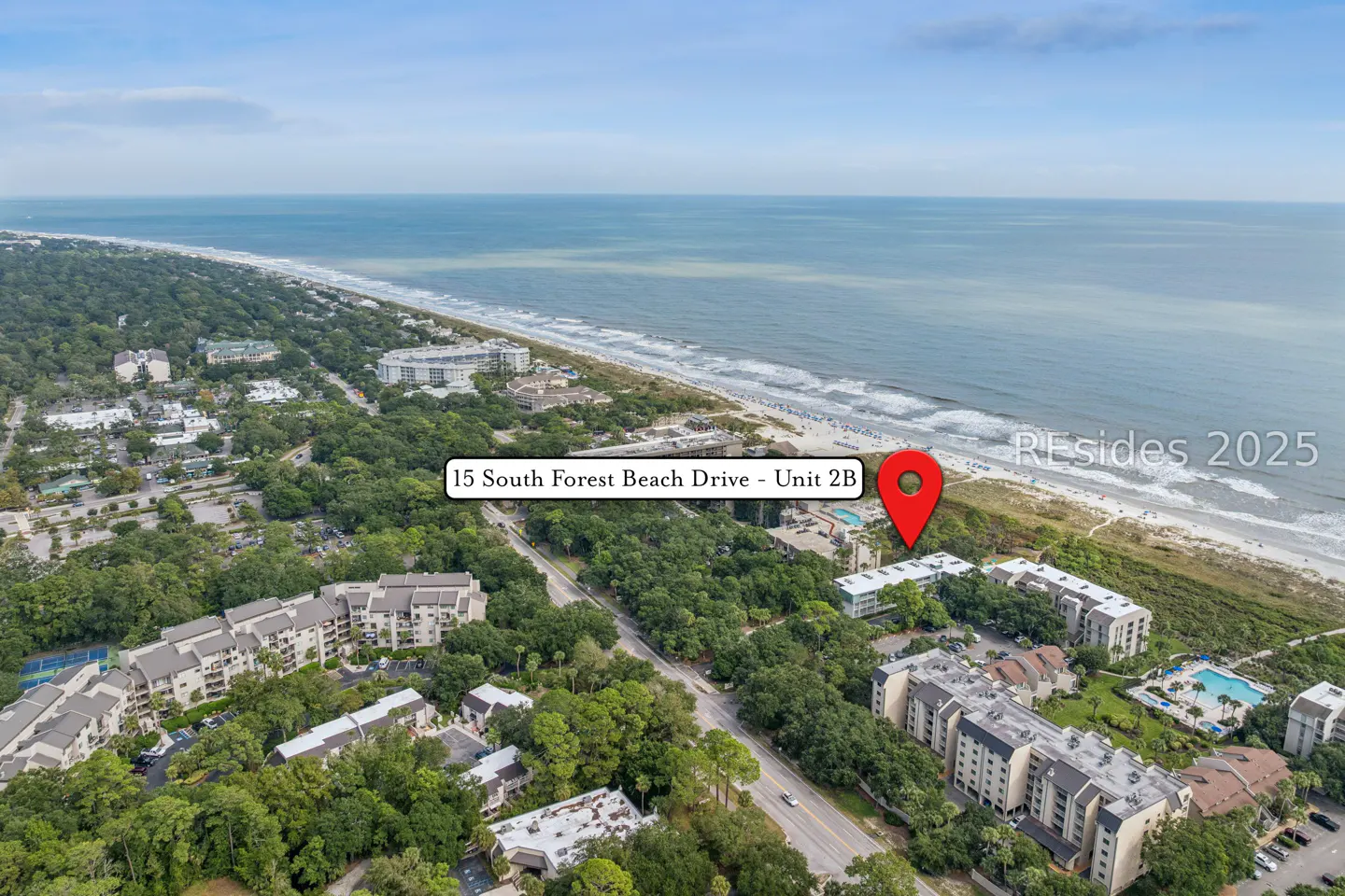 Aerial view of 15 South Forest Beach Drive, Unit 2B, near the beach. Condos are surrounded by green trees. Ocean in the background.