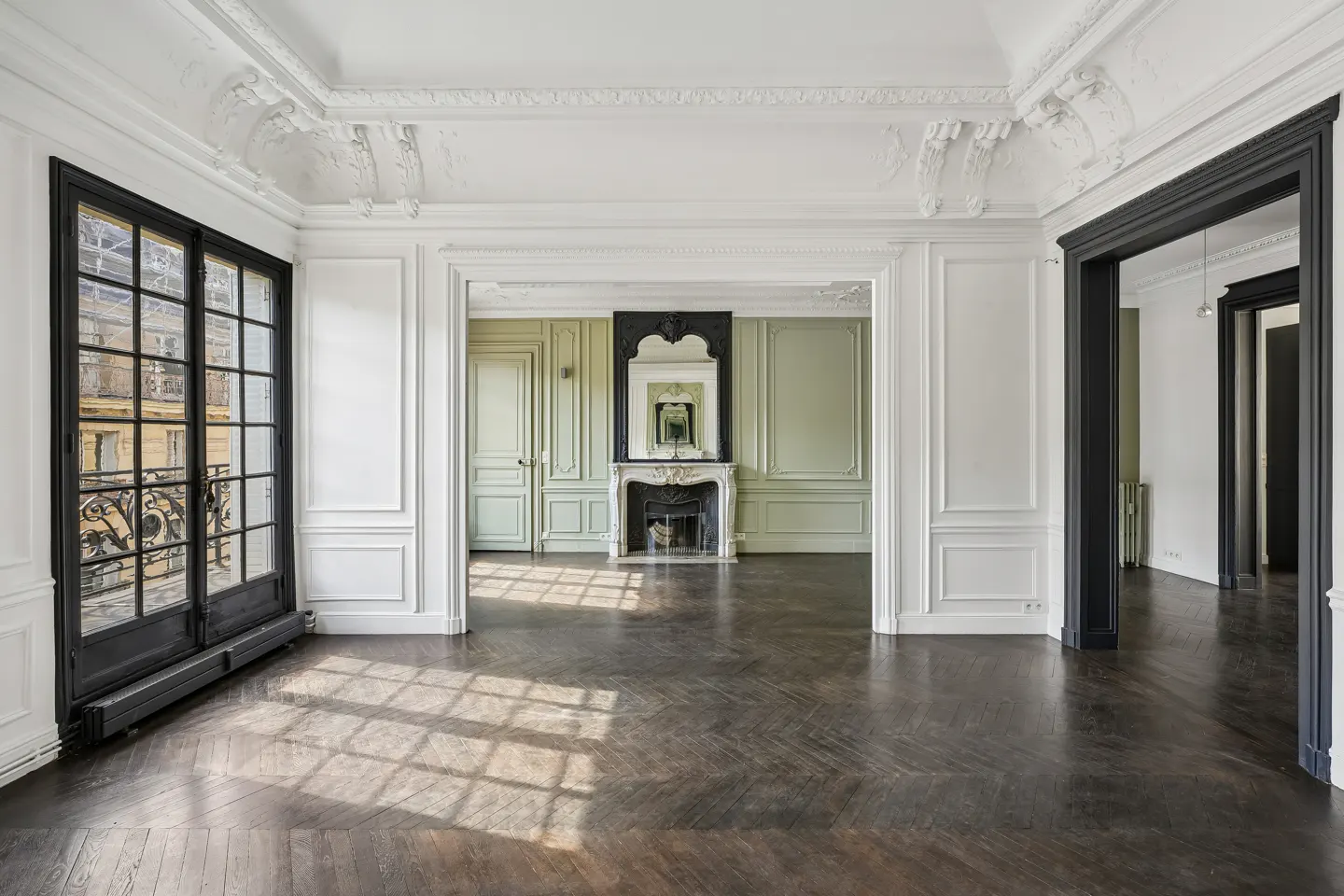 An empty room with dark wood floors, white walls, and black door frames. A fireplace is visible in the background.